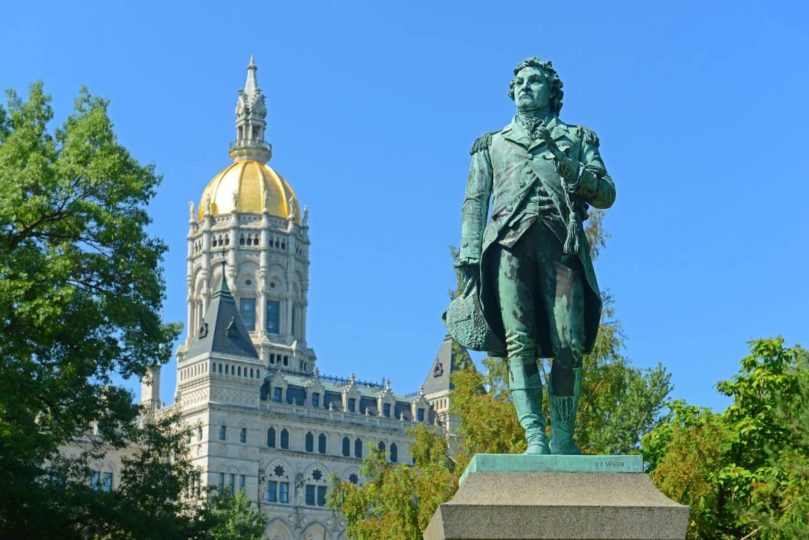 Bronze statue of General Lafayette standing in front of the Connecticut State Capitol in Hartford, with the building’s gold-domed tower and blue sky in the background.